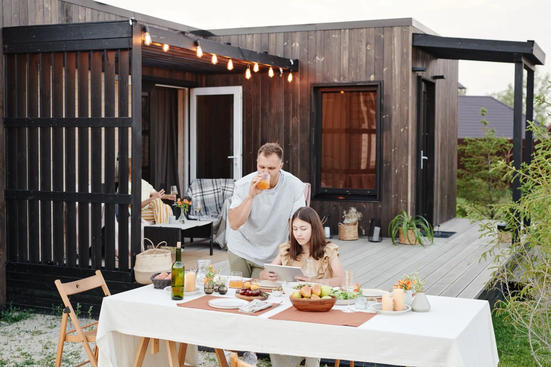 Family eating at a long table on a deck under strung lights
